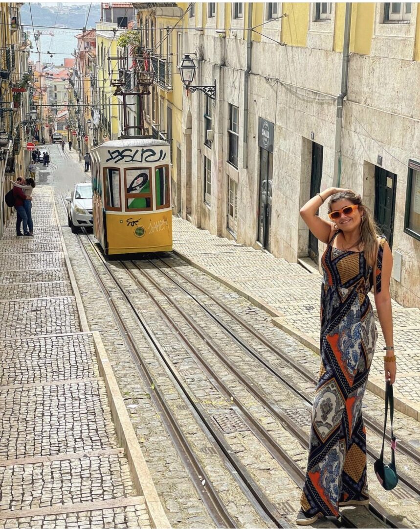 Κοπέλα που ποζάρει μπροστά από ένα κ'κίτρινο τραμ σε πεζόδρομο στη Λισαβόνα