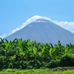 To ηφαίστειο Ometepe στη Νικαράγουα από μακρινή απόσταση τη μέρα και μπροστά πράσινες φυλλωσιές από μπανανιές
