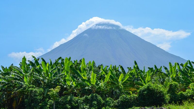 To ηφαίστειο Ometepe στη Νικαράγουα από μακρινή απόσταση τη μέρα και μπροστά πράσινες φυλλωσιές από μπανανιές
