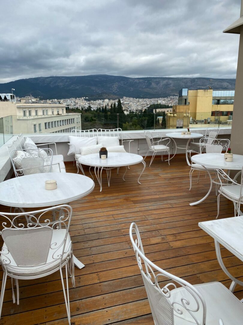 Ταράτσα με ξύλινο πάτωμα και λευκά τραπεζοκαθίσματα με θέα το βουνό και την πόλη της Αθήνας