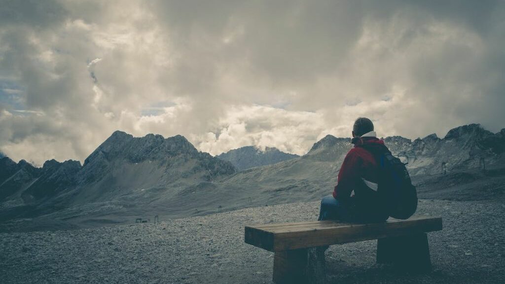 Άνδρας που κάθεται σε ένα ξύλινο παγκάκι και κοιτάζει τα βουνά