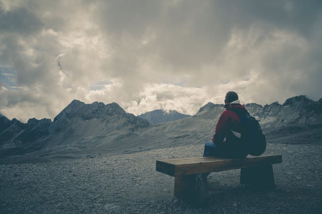 Άνδρας που κάθεται σε ένα ξύλινο παγκάκι και κοιτάζει τα βουνά
