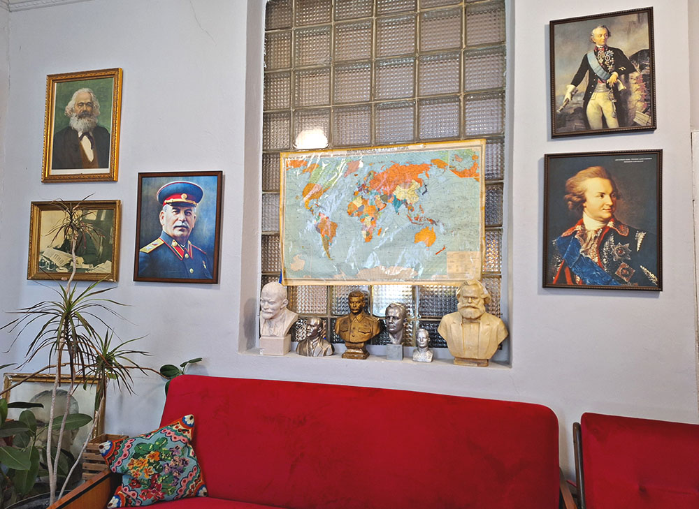Kόκκινος καναπές και στον τοίχο κρεμασμένες εικόνες πολιτικών προσώπων και παγκόσμιος πολιτικός χάρτης