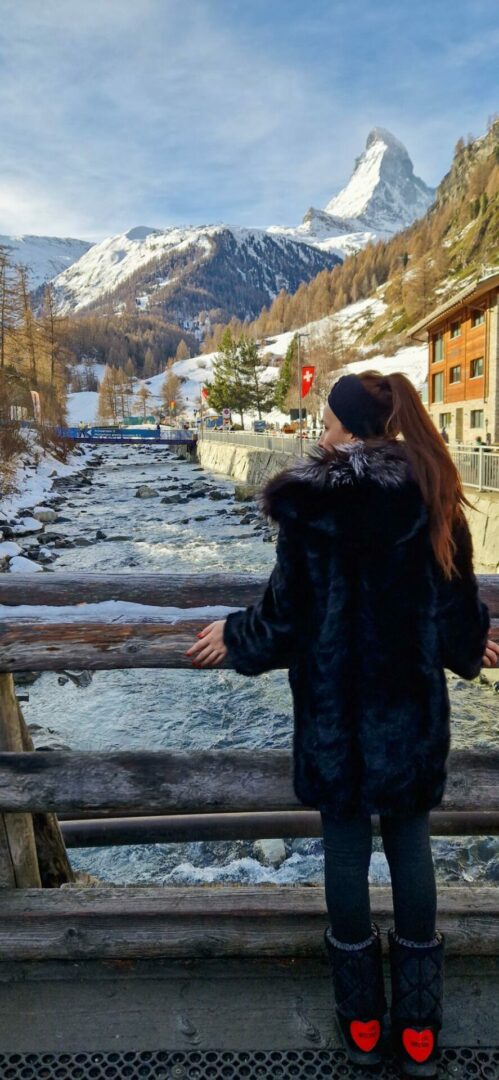 Κοπέλα που κοιτάει ένα ποτάμι και το χιονισμένο τοπίο στο βάθος