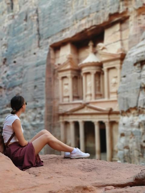 Κοπέλα καθισμένη σε βράχια, κοιτάζοντας έναν αρχαίο ναό