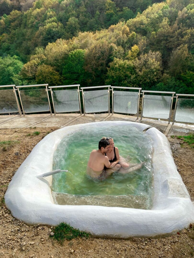 Ζευγάρι που κάνει μπάνιο σε πισίνα με ιαματικά νερά και πίσω δάσος