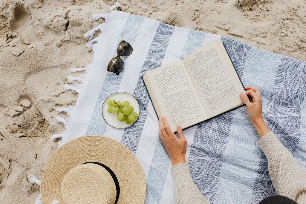 Βιβλίο πάνω σε πετσέτα θαλάσσης, άμμος από κάτω και γυαλιά ηλίου