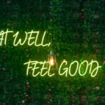Φωτεινή επιγραφή σε πράσινο φόντο, γραμμένη η φράση με πράσινα γράμματα νέον η φράση ''eat well feel good''