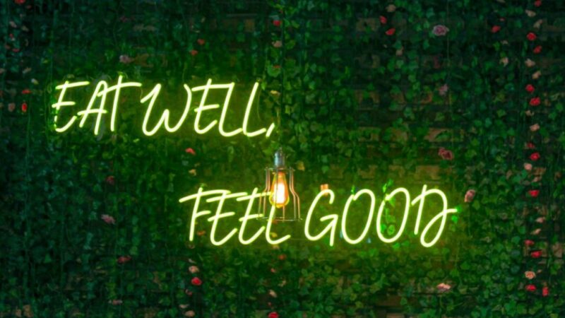 Φωτεινή επιγραφή σε πράσινο φόντο, γραμμένη η φράση με πράσινα γράμματα νέον η φράση ''eat well feel good''