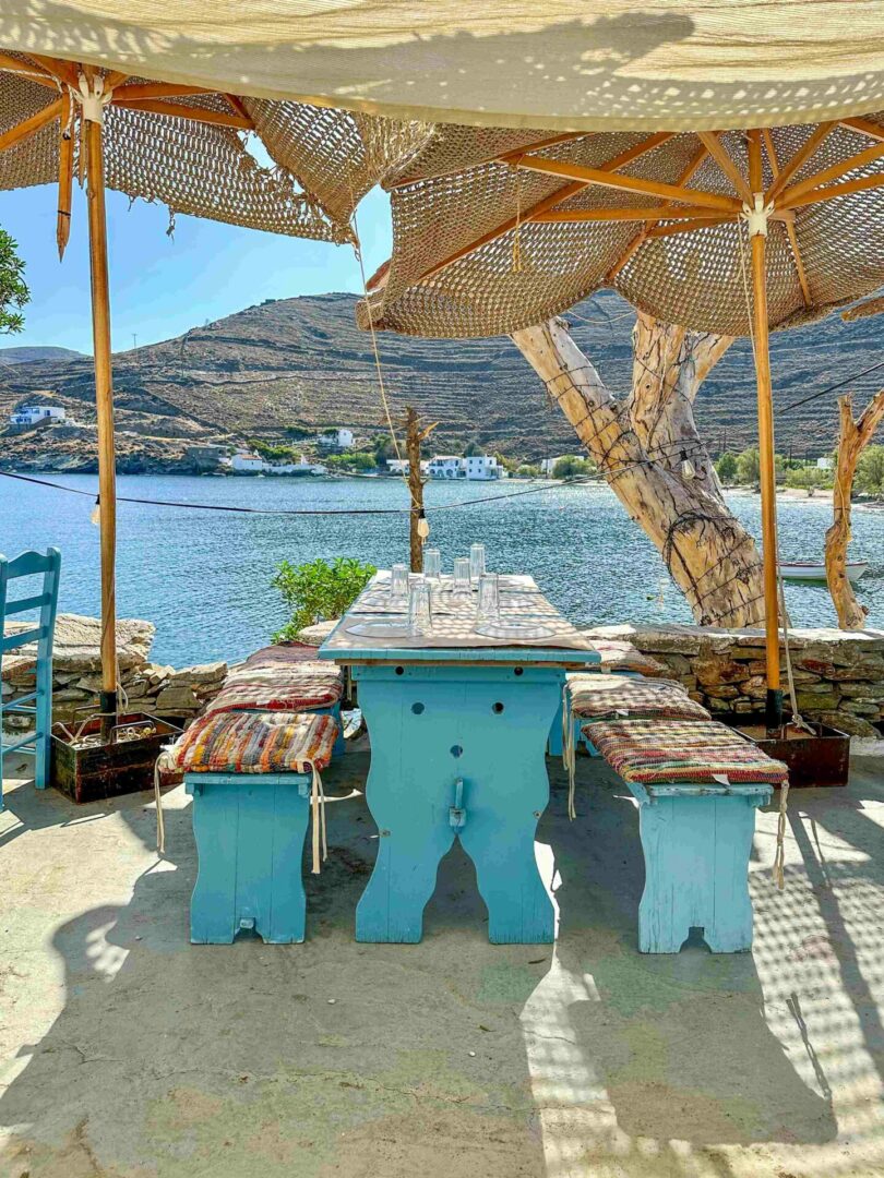 Μπλε ξύλινο τραπέζι με καρεκλάκια, ομπρέλες και θέα τη θάλασσα