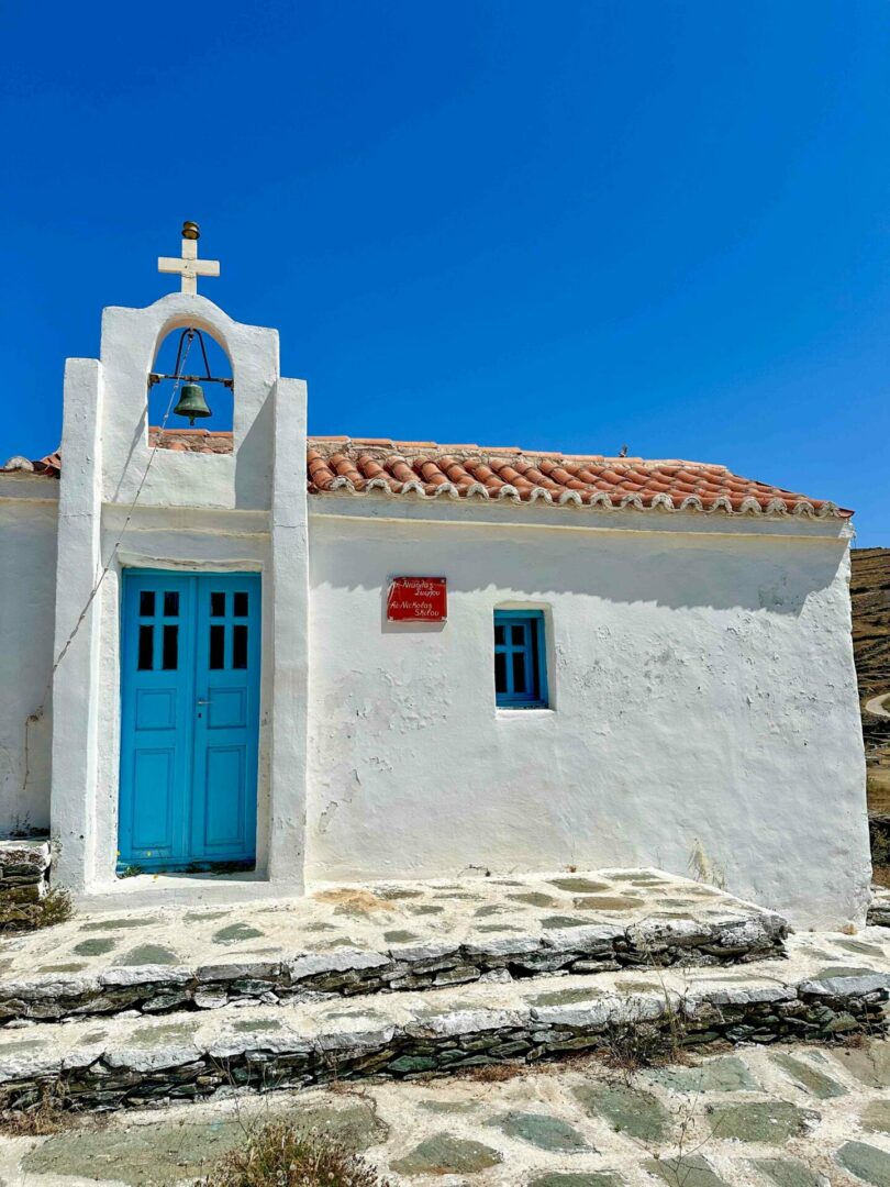 Λευκό κυκλαδίτικο εκκλησάκι με μπλε πόρτα και μικρό καμπαναριό
