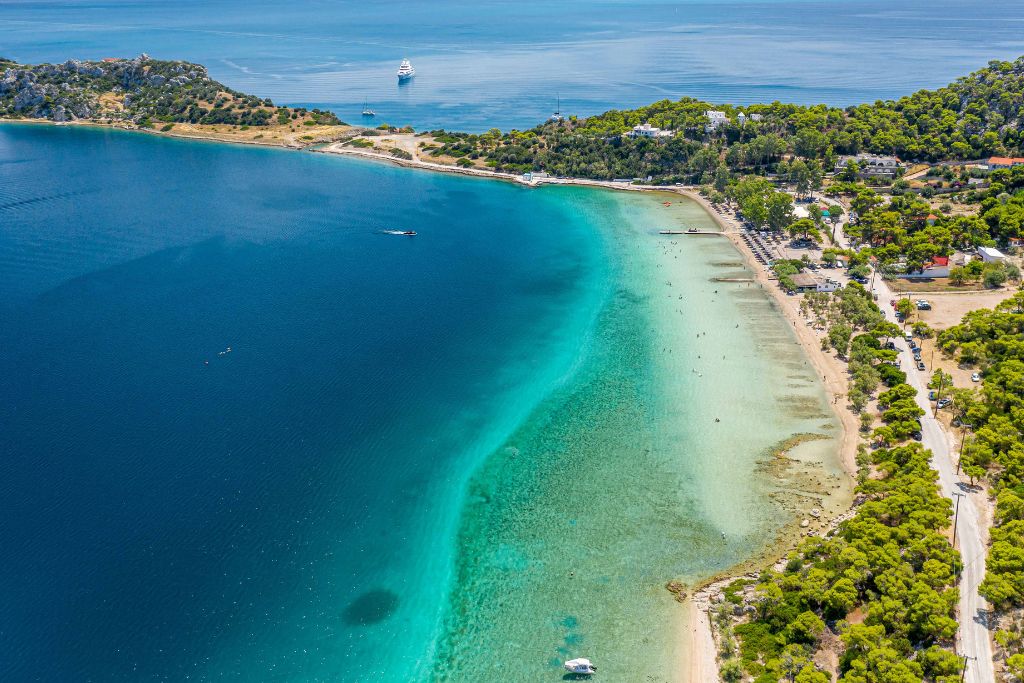 Παραλία με άμμο, δέντρα πίσω της και γαλαζοπράσινα νερά