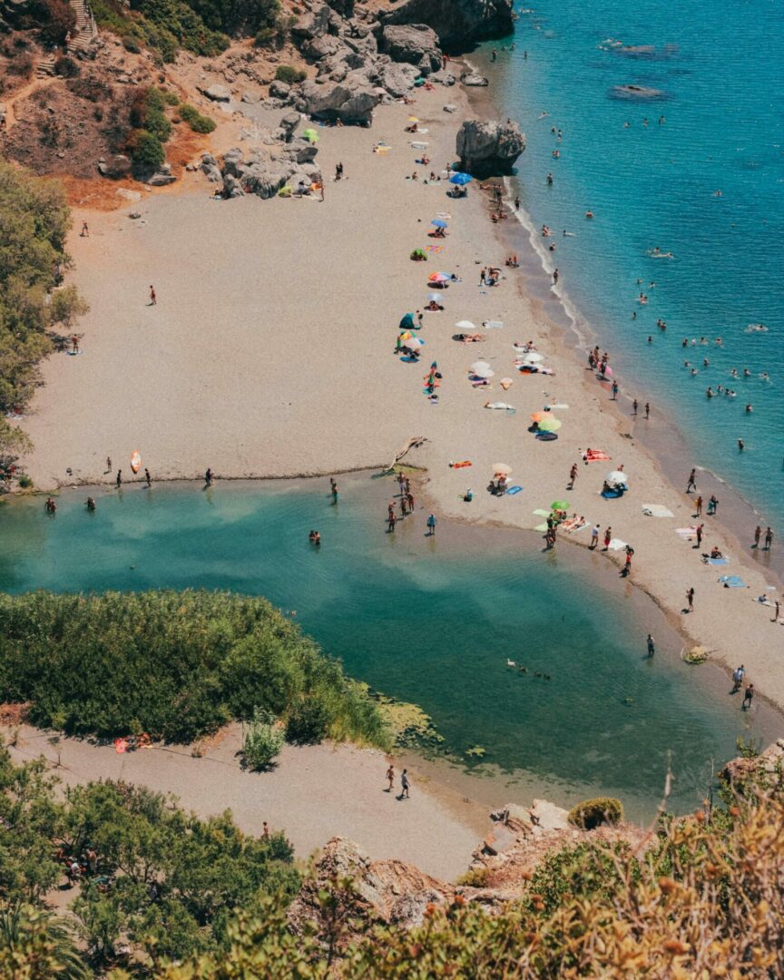 Παραλία από ψηλά με άμμο και πολύ κόσμο. Πίσω υπάρχουν βράχια και βλάστηση