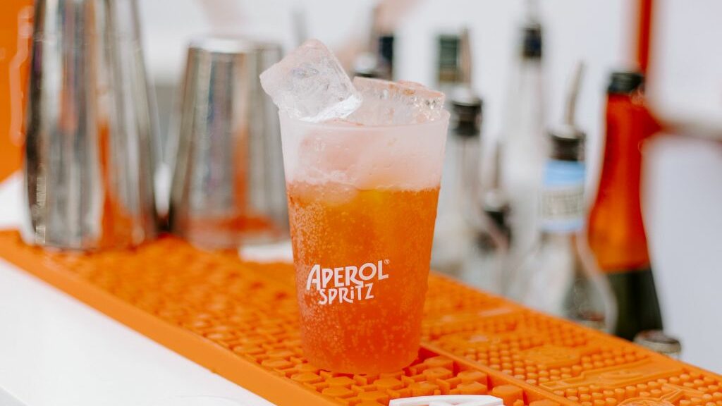 Ποτήρι aperol spritz σε πορτοκαλί χρώμα και πίσω μπουκάλια και ποτήρια