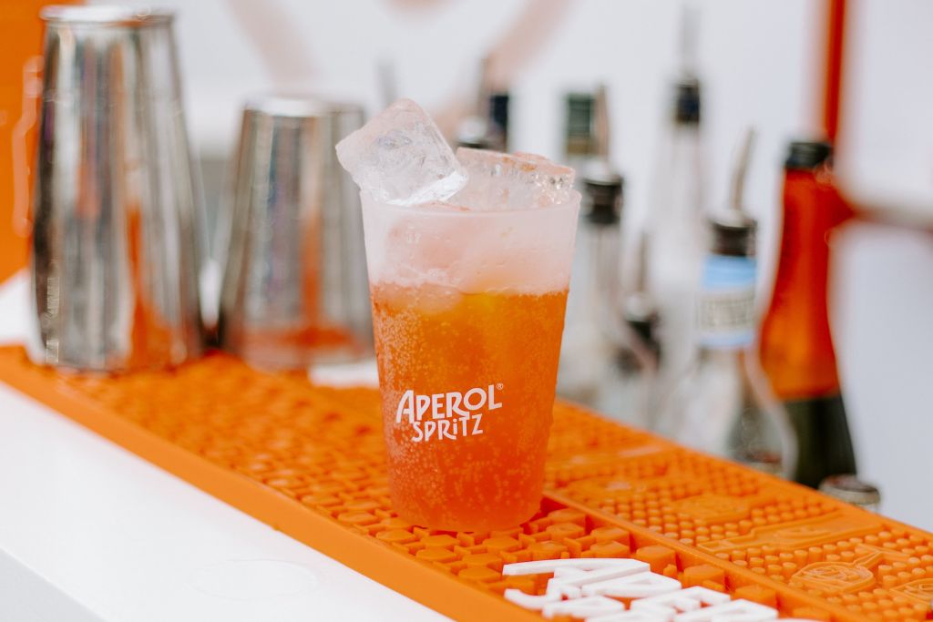 Ποτήρι aperol spritz σε πορτοκαλί χρώμα και πίσω μπουκάλια και ποτήρια