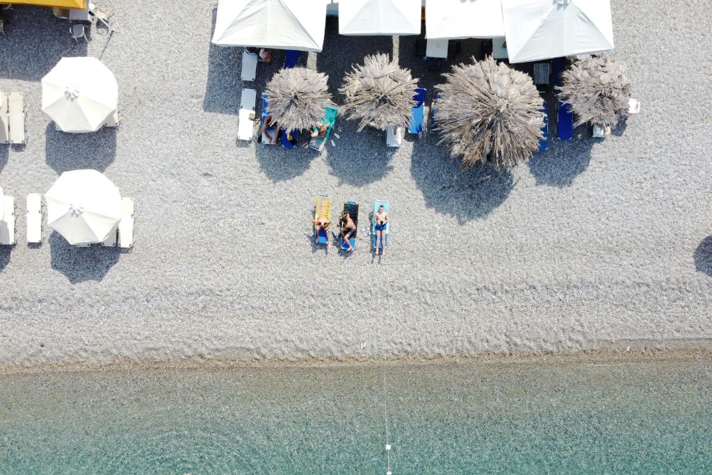 Παραλία με ομπρέλες από ψηλά και λουόμενοι πάνω σε ξαπλώστρες