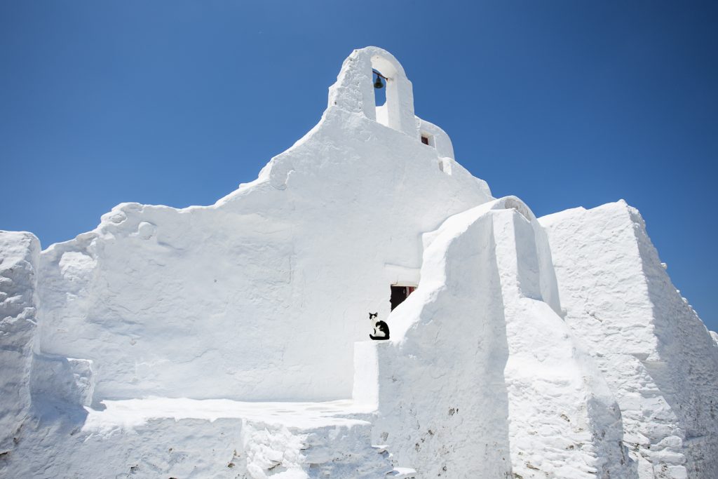 Λευκό εκκλησάκι με μικρό καμπαναριό ψηλά κάτω από γαλανό ουρανό