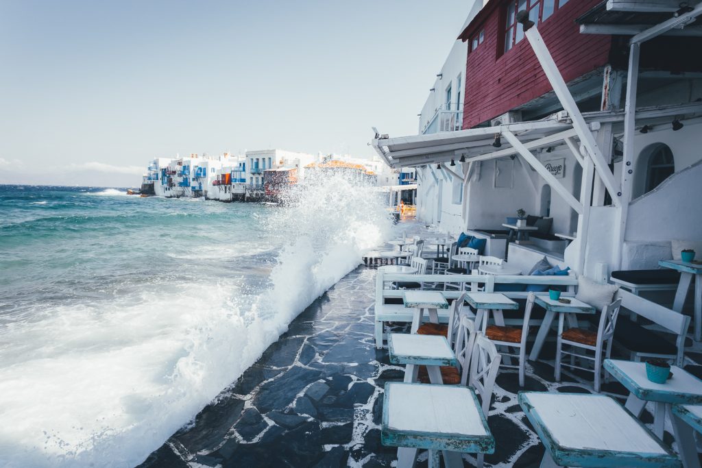 Παφλασμός κυμάτων πάνω σε παραθαλάσσιο σοκάκι με λευκά τραπεζοκαθίσματα