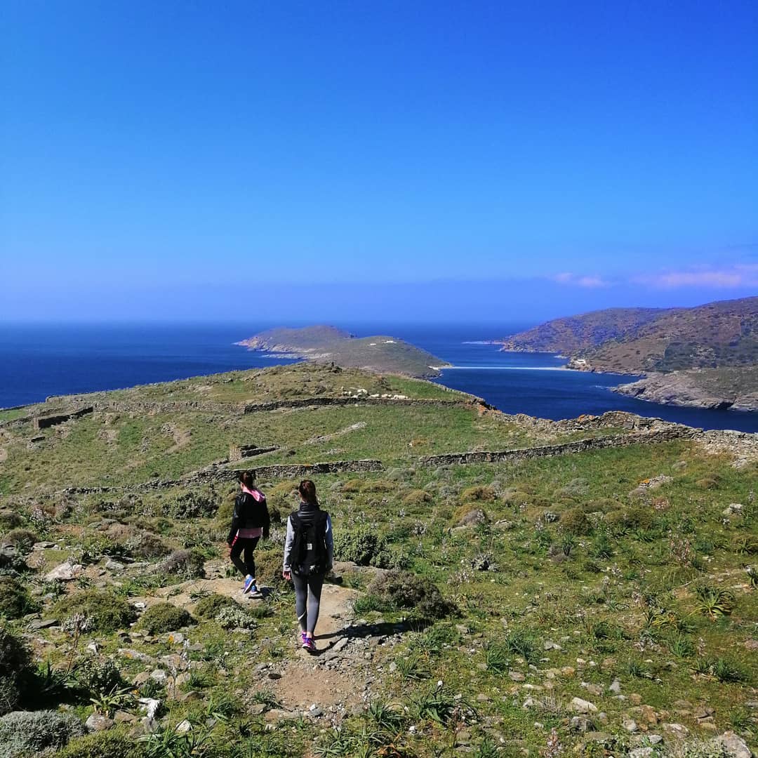 2 άνθρωποι περπατάνε σε μονοπάτι σε νησί με θέα θάλασσα